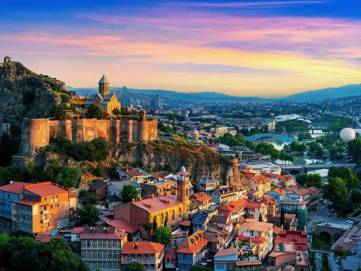 Vista de Tbilisi ao entardecer, com fortaleza, igrejas e o rio Kura