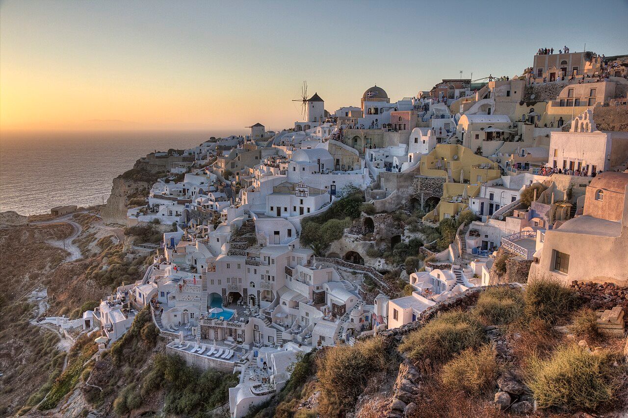 Casas de Oia na encosta de Santorini, com o mar ao fundo ao entardecer.