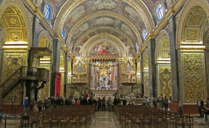 Nave da Co-Catedral de São João, em Valletta, com lápides de mármore colorido no piso e decoração dourada.
