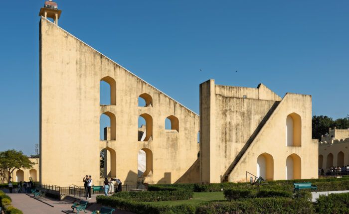 Estrutura triangular com arcos do Vrihat Samrat Yantra, no Jantar Mantar de Jaipur, com jardins e visitantes à frente.