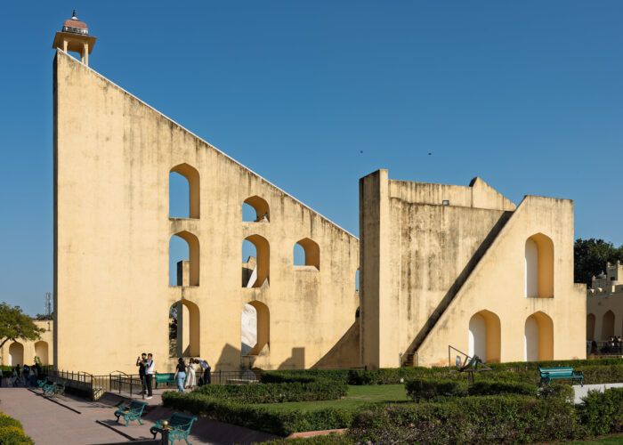 Estrutura triangular com arcos do Vrihat Samrat Yantra, no Jantar Mantar de Jaipur, com jardins e visitantes à frente.