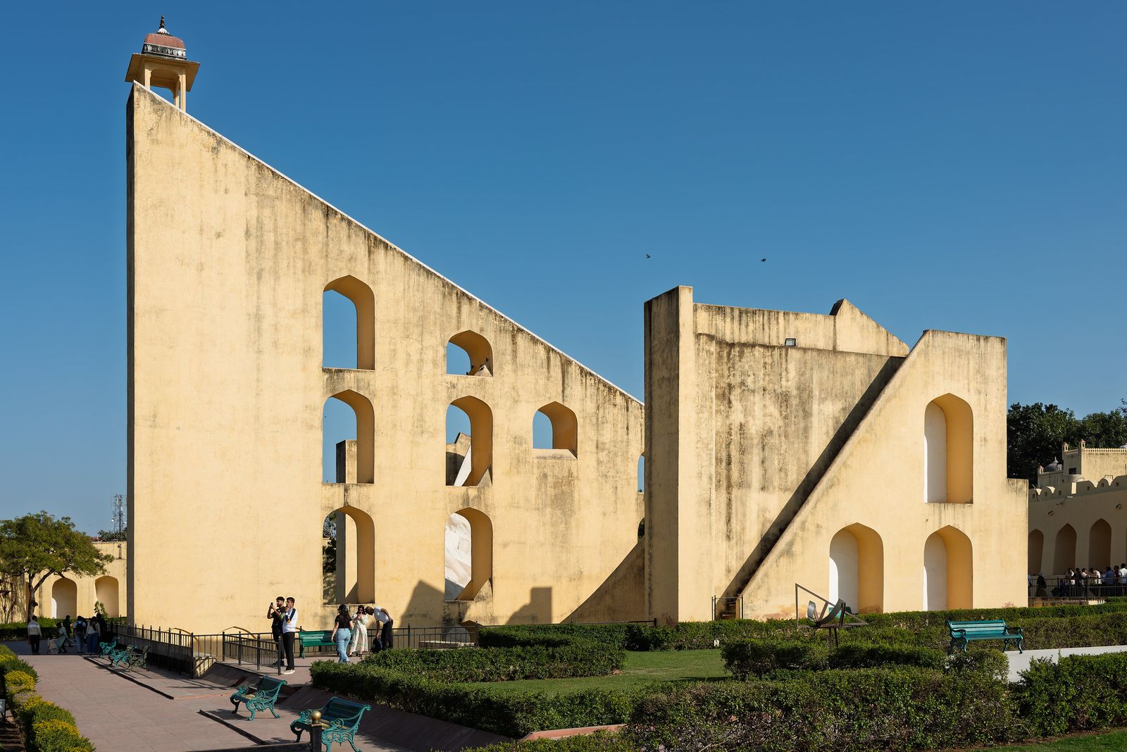 Estrutura triangular com arcos do Vrihat Samrat Yantra, no Jantar Mantar de Jaipur, com jardins e visitantes à frente.