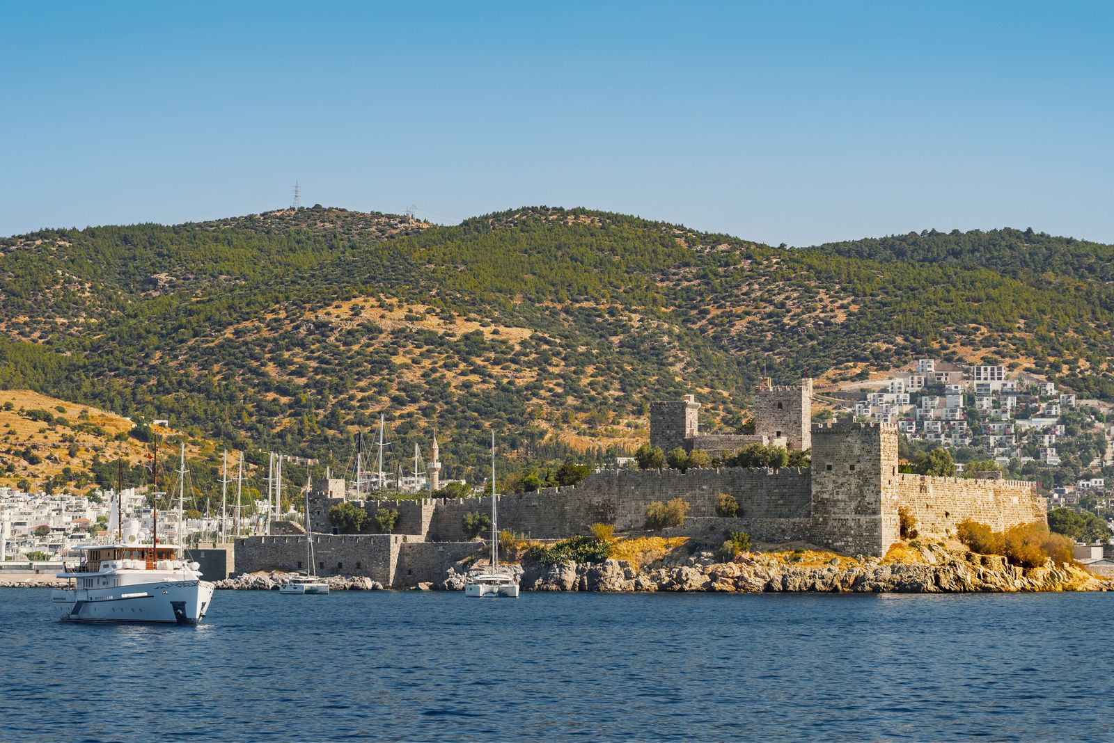 Castelo de Bodrum junto ao mar, com colinas ao fundo e embarcações na baía.