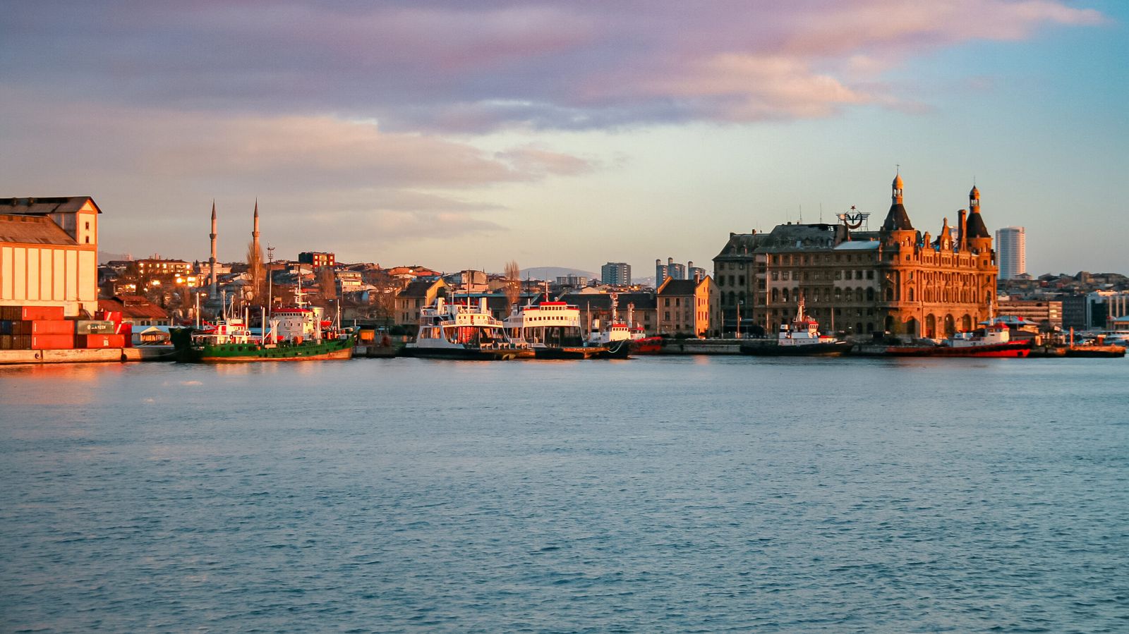 Orla de Kadıköy em Istambul ao entardecer, com o edifício de Haydarpaşa e barcos atracados.