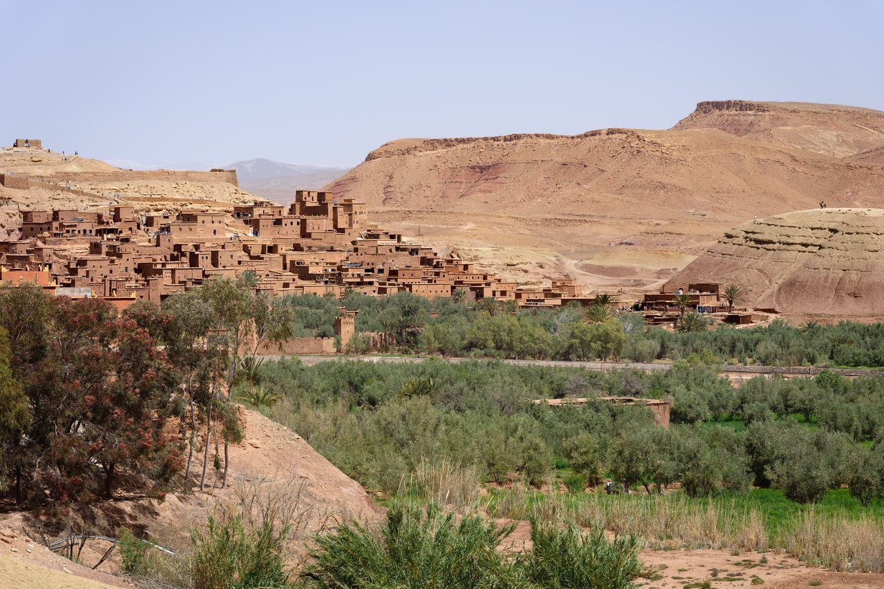 Construções de terra de Aït Ben Haddou diante de colinas áridas e vegetação no vale.