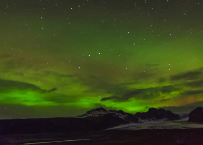 Aurora boreal sobre montanhas e geleira na Islândia