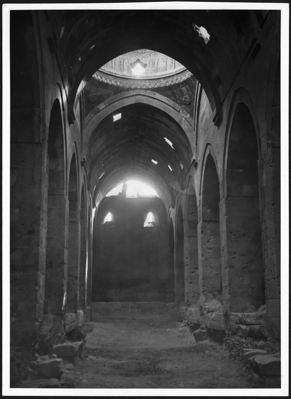Fotografia em preto e branco do salão de Sultan Han, com arcos, pilares e cobertura abobadada, em 1933–1934.
