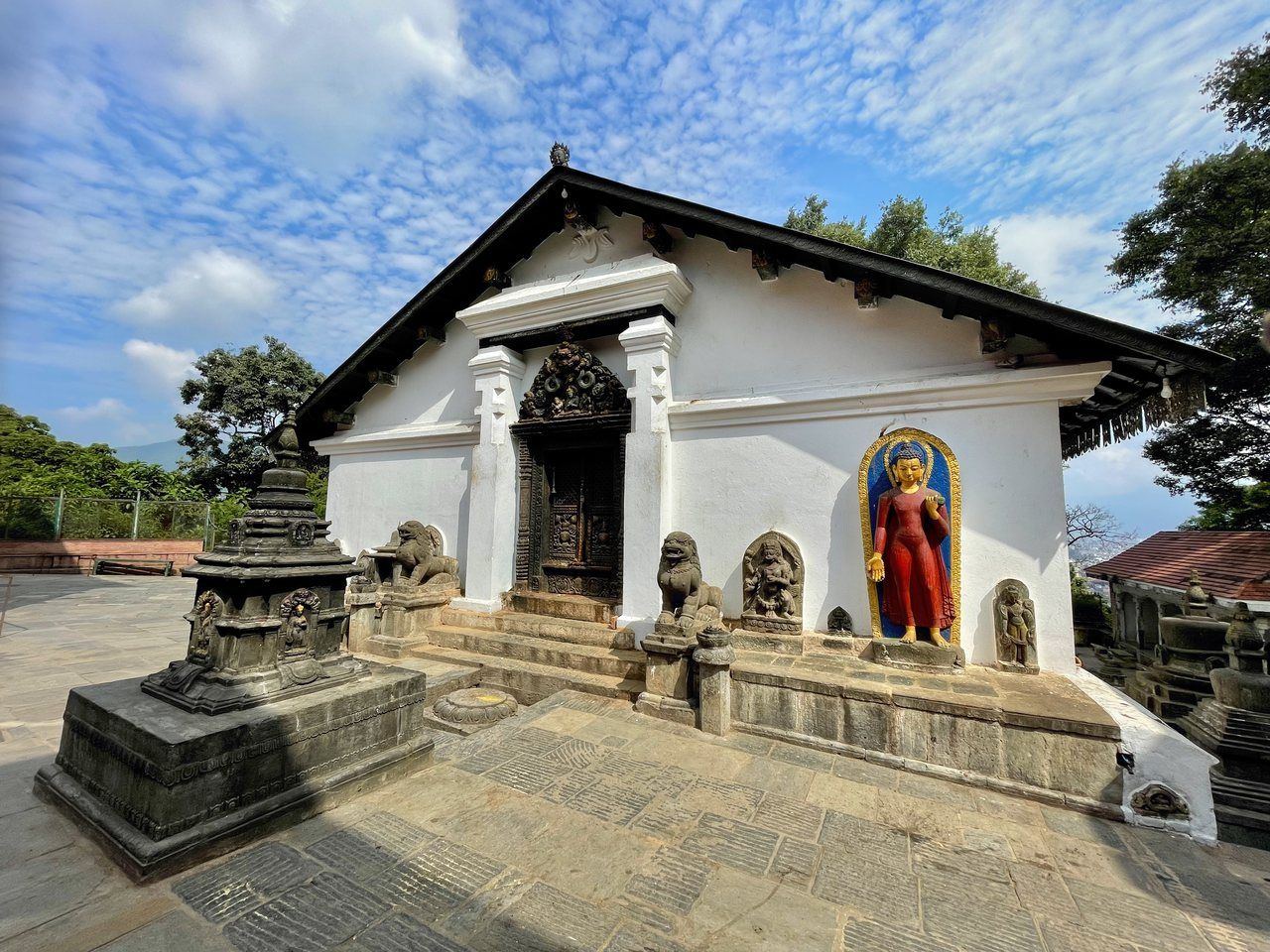 Santuário Shantipur no complexo Swayambhunath, com paredes brancas, portal entalhado e esculturas no pátio.