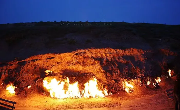 Chamas de Yanar Dag iluminam a base de uma encosta ao entardecer, no Azerbaijão.